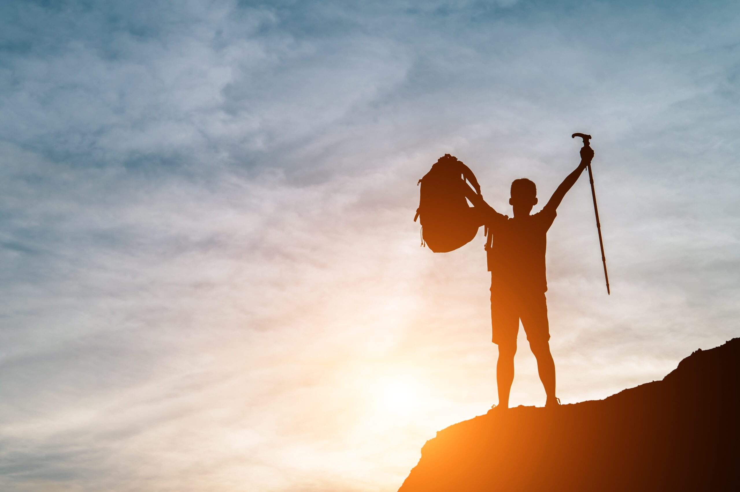 Silhouette of a triumphant hiker holding gear atop a mountain at sunrise, symbolizing achievement in meeting transfer pricing documentation requirements.